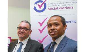 John McGowan and Professor Jermaine Ravalier stand in front of a "Campaigning for better working conditions and wellbeing for social workers" poster
