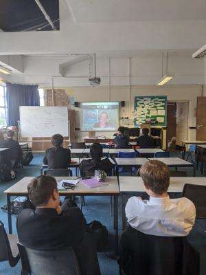 Year 10 students sit at their desks in a classroom. They are looking at a projector screen showing the Zoom call with SWU General Secretary John McGowan for the Shout Out UK workshop on social work and trade unions.